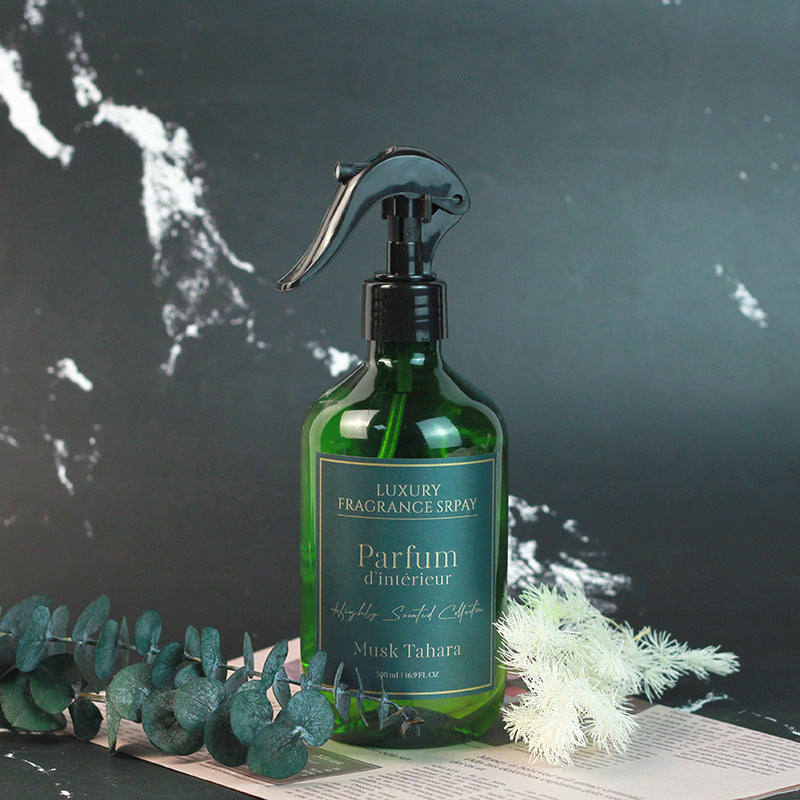 Green fragrance spray bottle labeled 'Parfum d'Intérieur' on a dark surface with greenery.