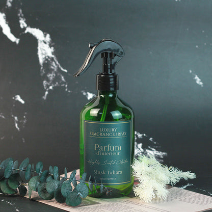 Green fragrance spray bottle labeled 'Parfum d'Intérieur' on a dark surface with greenery.