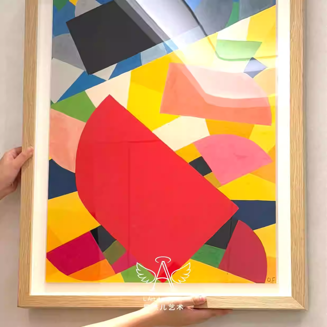 Colorful abstract art piece with geometric shapes in a wooden frame held by a person.