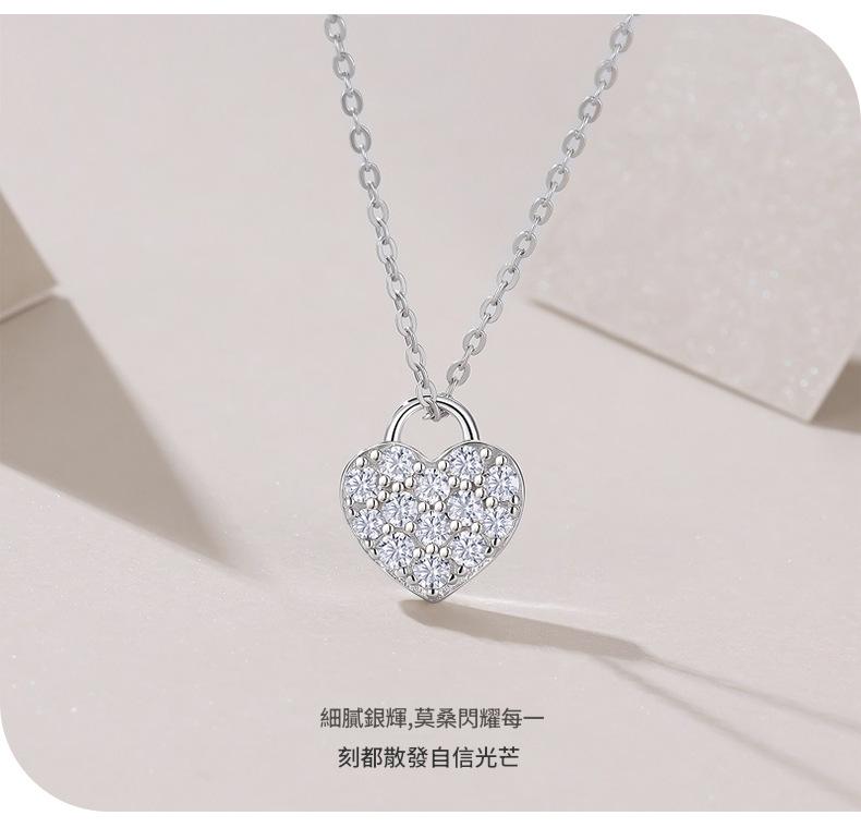 Heart-shaped silver necklace with clear stones on a light pink background