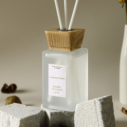 Frosted diffuser bottle with wooden cap on a stone surface, blurred background