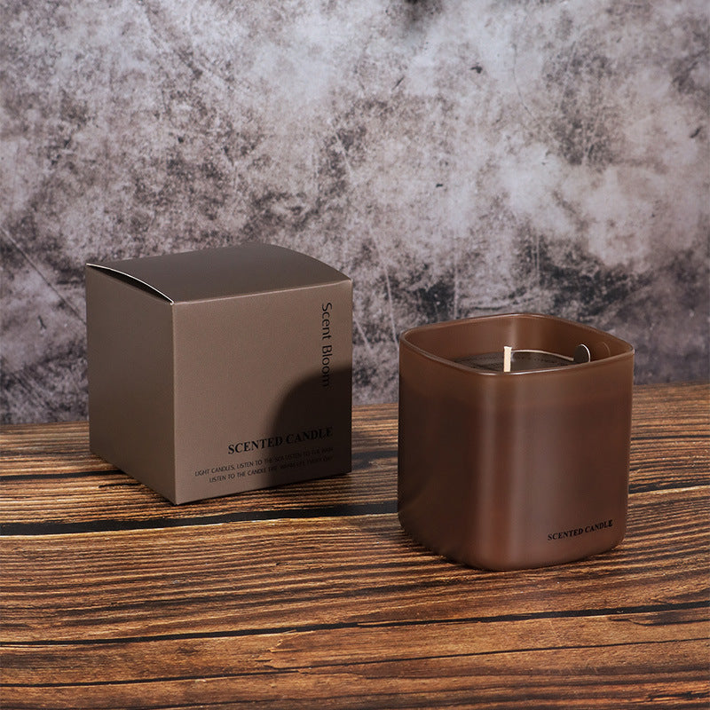 Brown scented candle and packaging on a wooden surface with a textured gray background