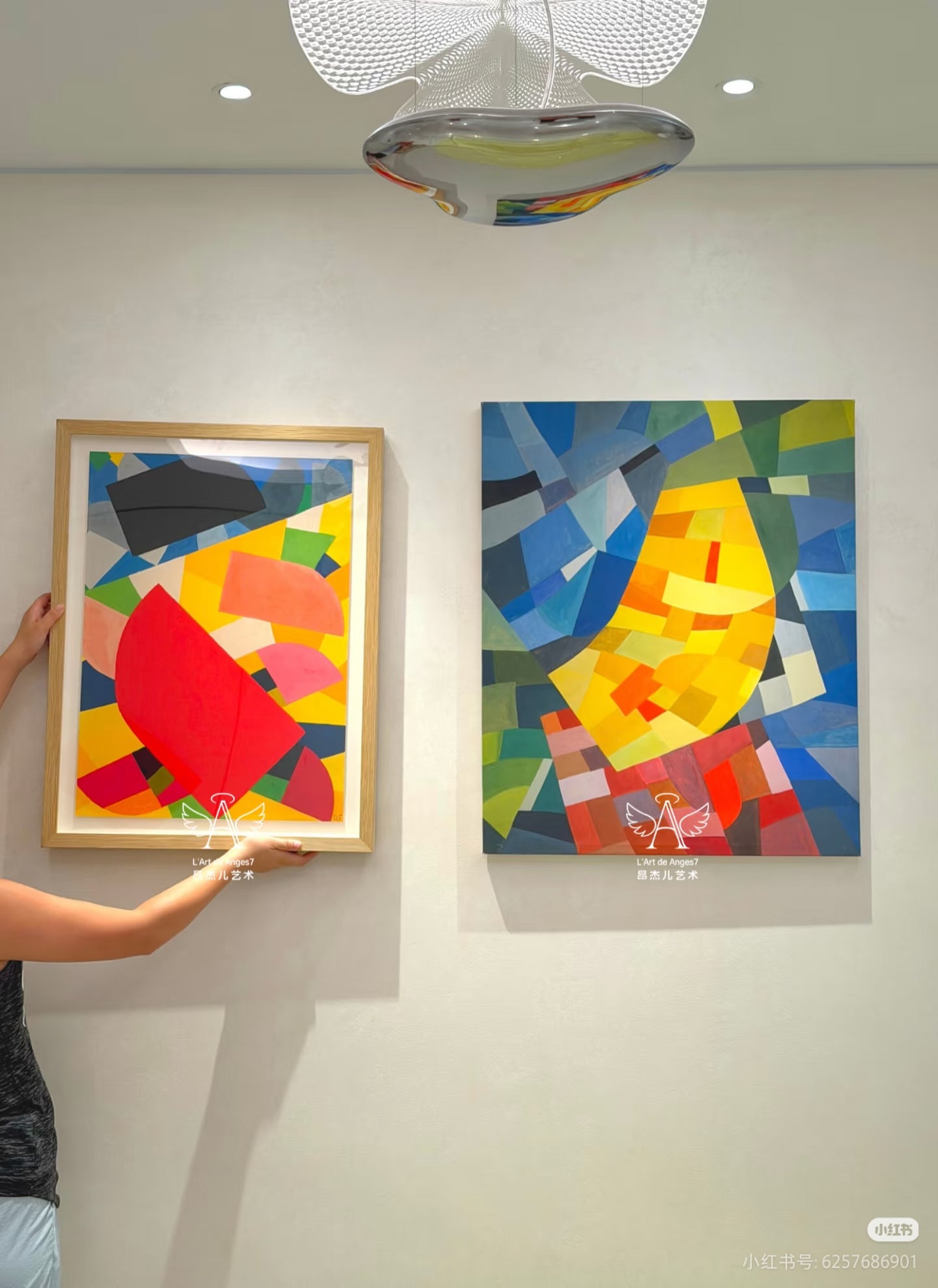 Two abstract artworks on a wall with a person adjusting one of them.