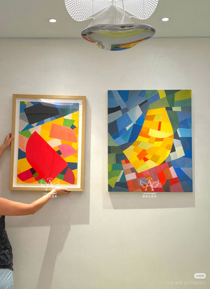 Two abstract artworks on a wall with a person adjusting one of them.
