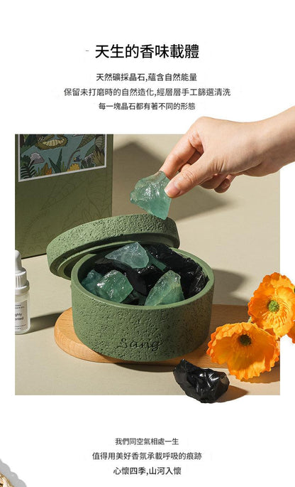 Green container with crystals, hand holding a crystal, and flowers on a light background