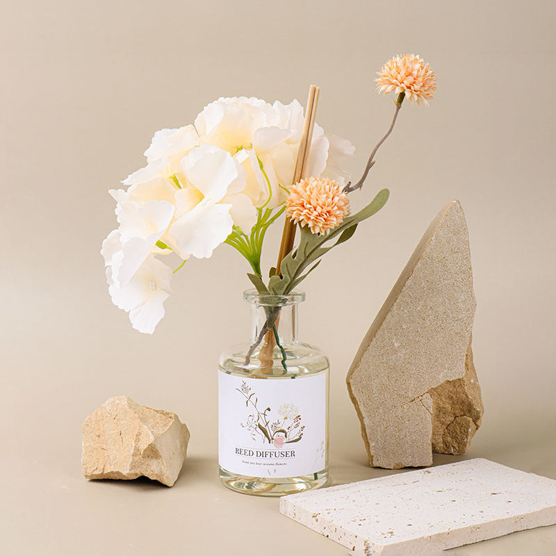 Glass diffuser bottle with flowers and rocks on a neutral background