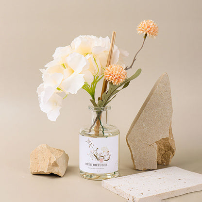 Glass diffuser bottle with flowers and rocks on a neutral background