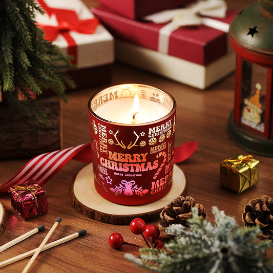 Red 'Merry Christmas' candle on a wooden coaster with holiday decorations.