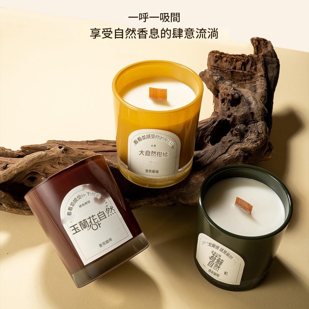 Three candles in different colored containers on a beige surface with wooden elements.