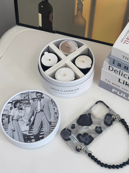 Set of mini candles in a tin with a keychain and photo album on a table.