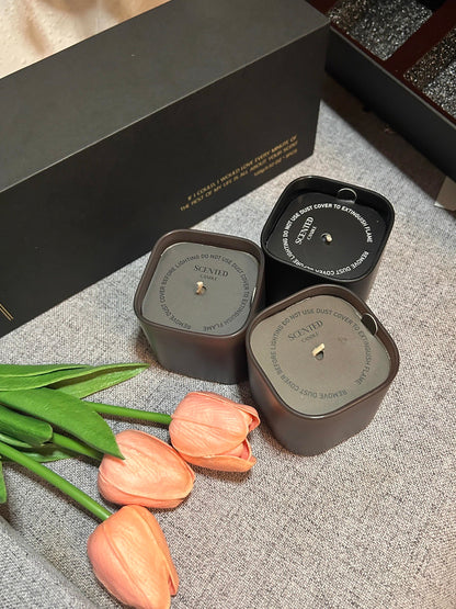 Two scented candles in black containers with pink tulips on a textured surface