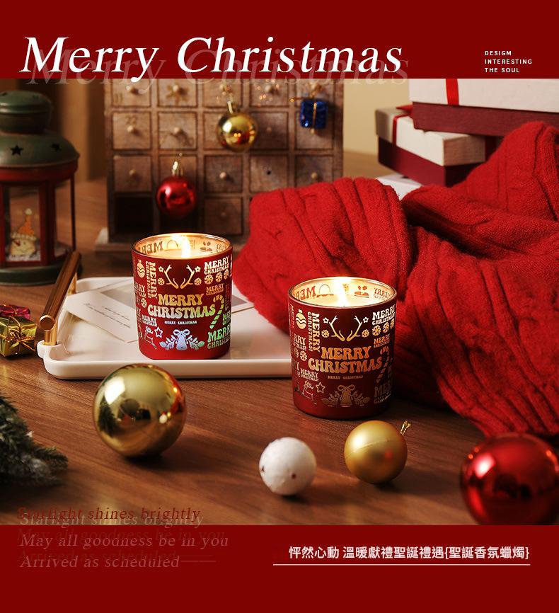 Two lit Christmas candles on a table with festive decorations and a red blanket.