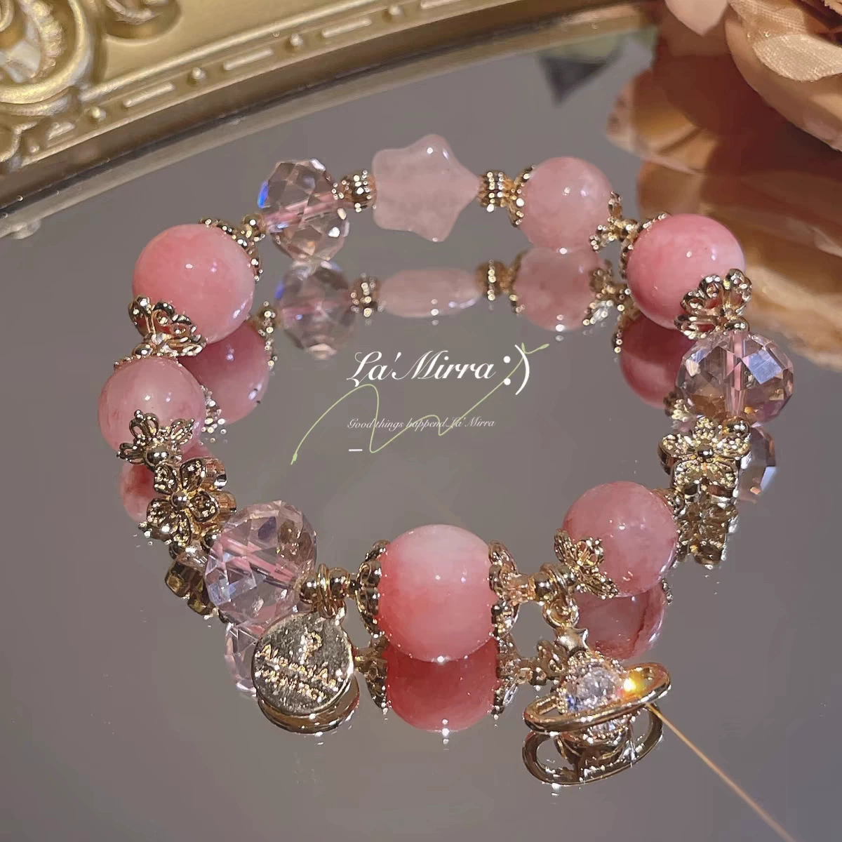 Pink beaded bracelet with gold accents on a reflective surface, featuring the brand 'La Mirra'.